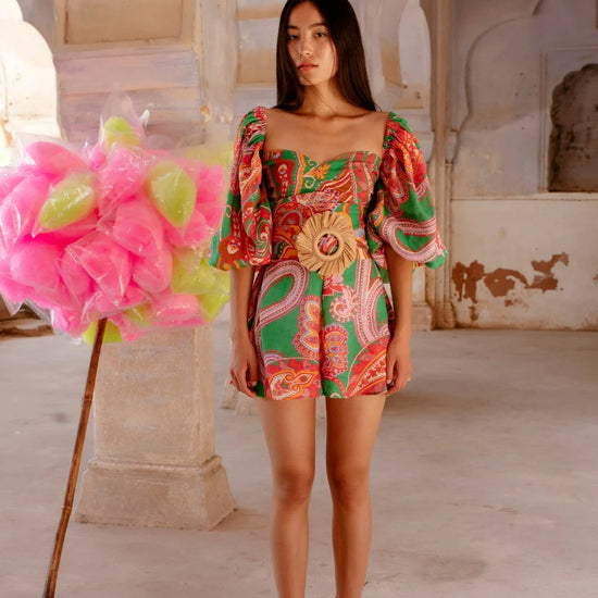 Green red and pink paisley print playsuit with oversized puff sleeves and a circle raffia belt