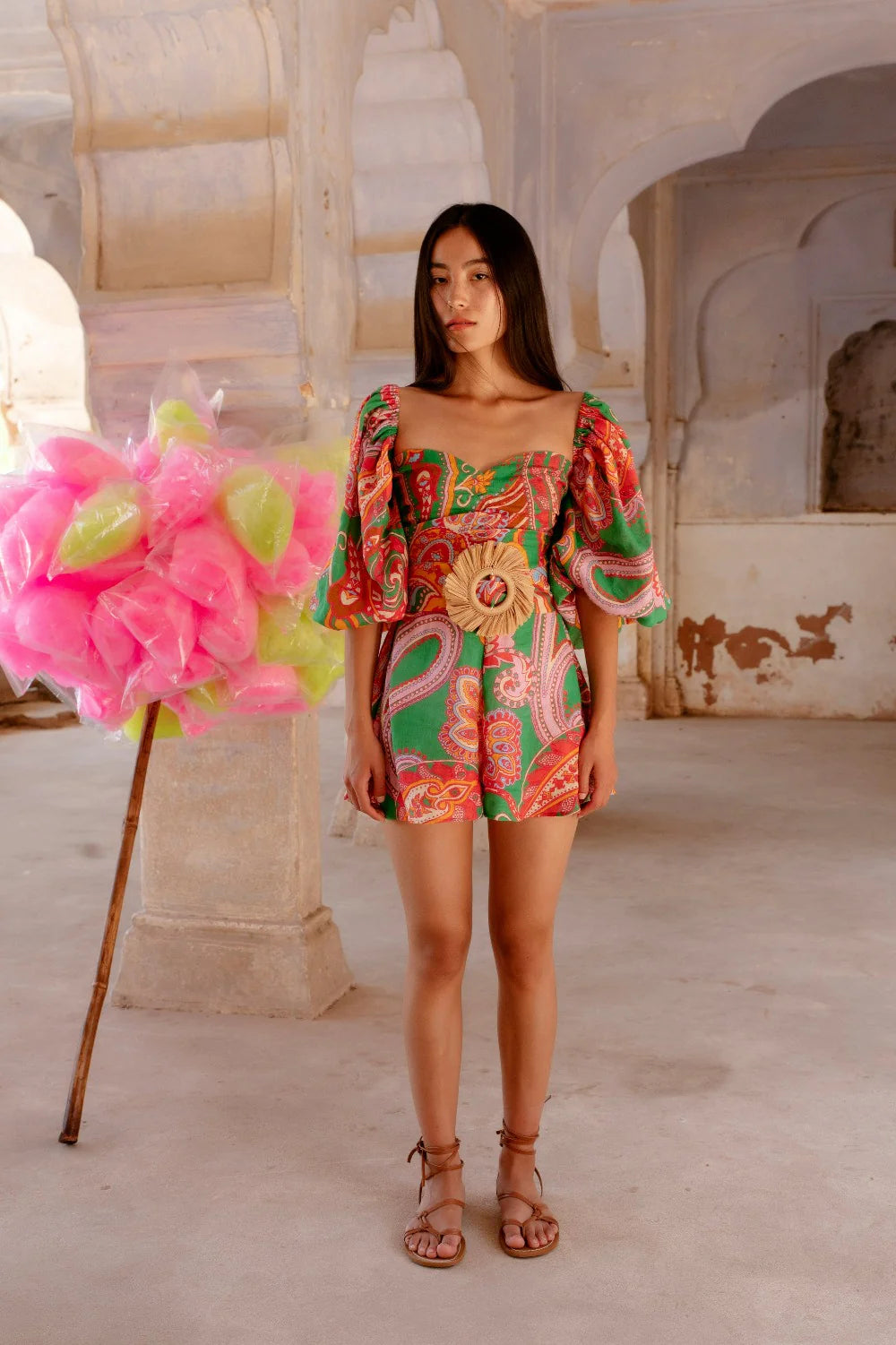 Green red and pink paisley print playsuit with oversized puff sleeves and a circle raffia belt