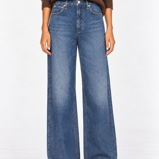 A model wearing a pair of wide-leg blue denim jeans, styled with a brown knit sweater and brown suede shoes, photographed against a clean white studio background.