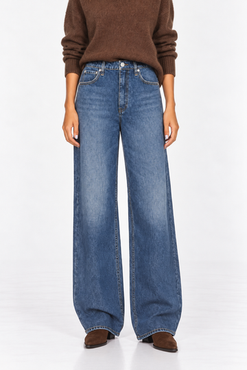 A model wearing a pair of wide-leg blue denim jeans, styled with a brown knit sweater and brown suede shoes, photographed against a clean white studio background.