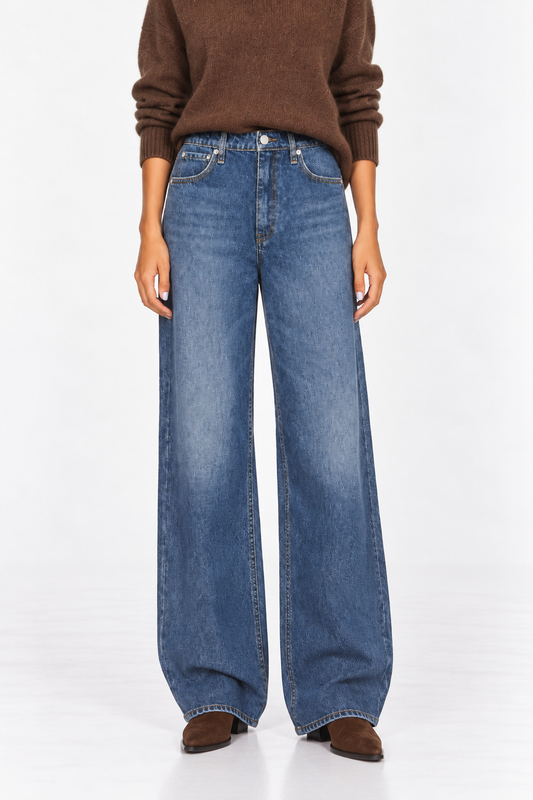 A model wearing a pair of wide-leg blue denim jeans, styled with a brown knit sweater and brown suede shoes, photographed against a clean white studio background.