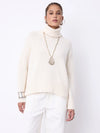 A woman modeling a cream-colored ribbed turtleneck sweater and white trousers against a plain white studio background.