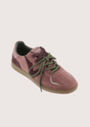 A low-top suede sneaker in dusty rose pink with olive green laces and a tan rubber sole, shown on a light beige background.