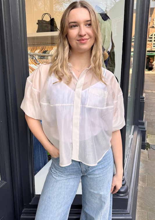 Woman wearing a sheer white blouse and light blue jeans.
