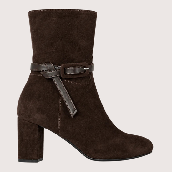 A dark brown suede ankle boot with a block heel and a matching brown leather strap detail around the ankle, shown against a light beige background.