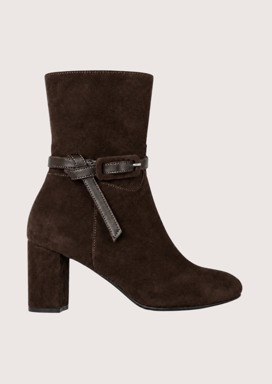 A dark brown suede ankle boot with a block heel and a matching brown leather strap detail around the ankle, shown against a light beige background.
