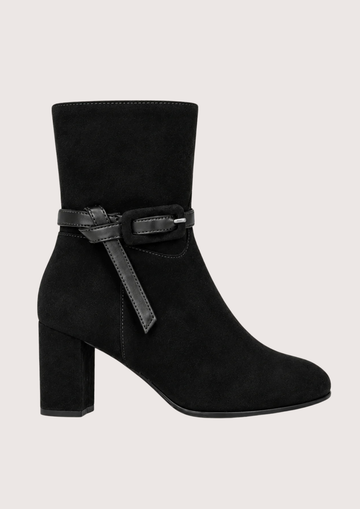 A black suede ankle boot with a block heel and a decorative black leather strap with a silver buckle around the ankle, shown against a light gray background.