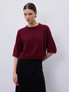 A woman modeling a short-sleeve crewneck sweater in deep burgundy, paired with a black skirt, against a plain light gray studio background.