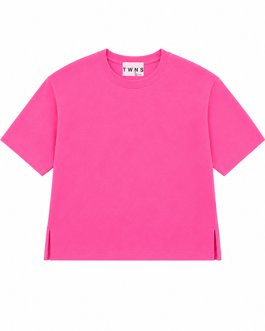 A bright pink short-sleeve crewneck t-shirt with side slits at the hem, displayed flat against a solid white background. The inner neck label shows the brand name 'TWN S'.