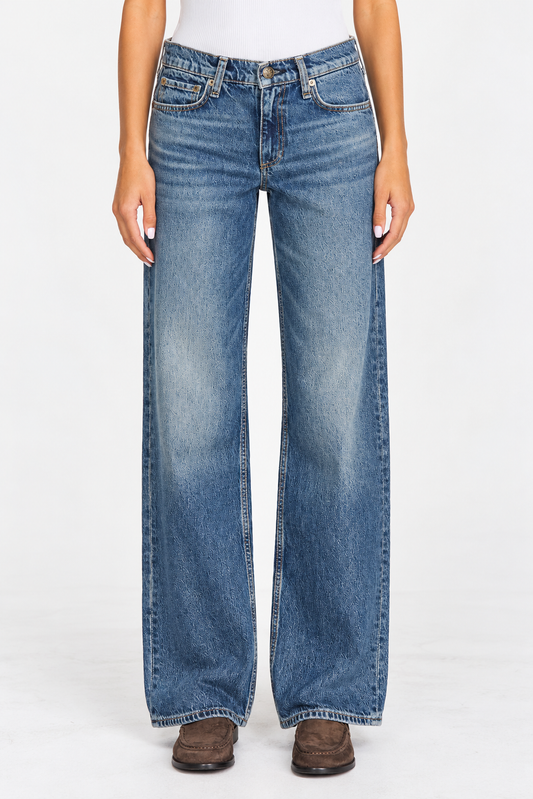 A person wearing a pair of wide-leg blue denim jeans with a faded wash, paired with brown shoes against a plain white studio background.