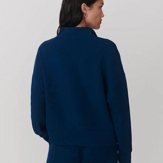 A woman shown from the back wearing a dark navy blue cropped sweatshirt and matching pants against a light gray studio background.