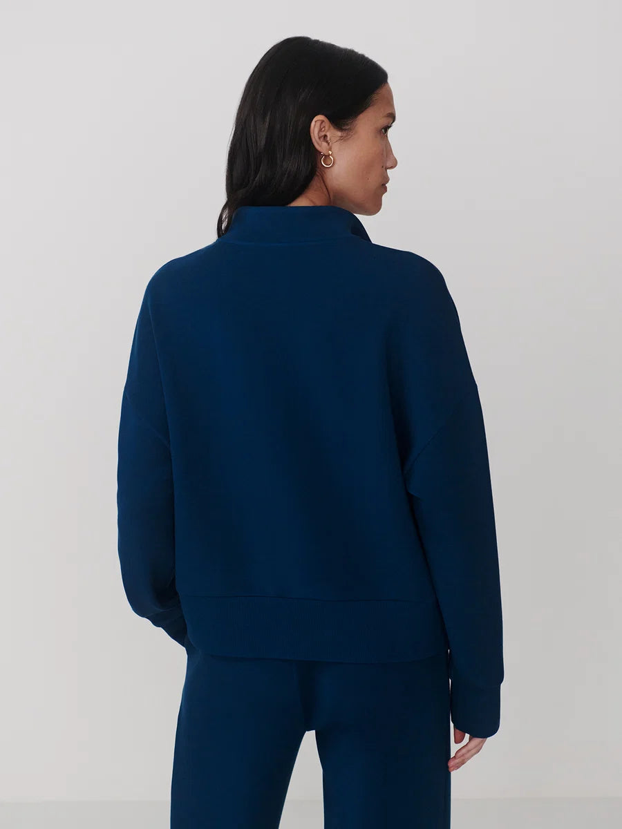 A woman shown from the back wearing a dark navy blue cropped sweatshirt and matching pants against a light gray studio background.