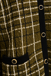 Close-up of a textured knit cardigan featuring an olive green, black, and cream plaid pattern, with a black ribbed trim and gold-tone metal grommets.