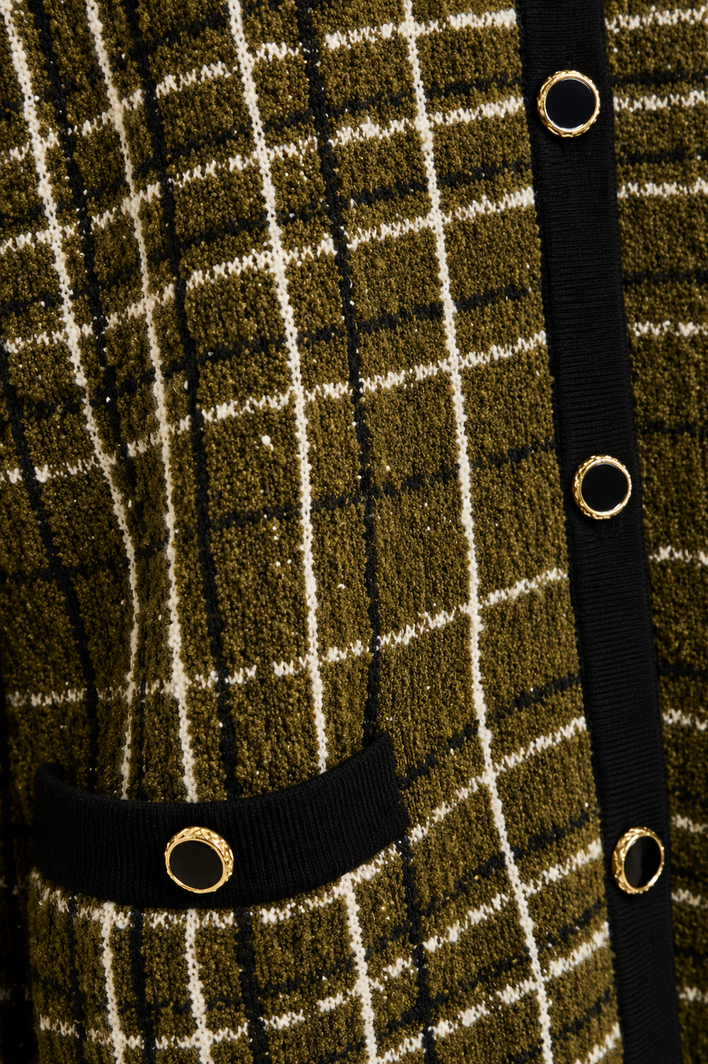 Close-up of a textured knit cardigan featuring an olive green, black, and cream plaid pattern, with a black ribbed trim and gold-tone metal grommets.