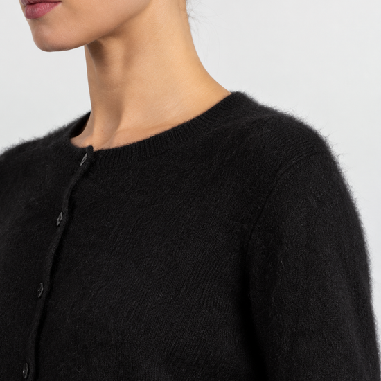 Close-up of a model wearing a fuzzy black knit cardigan sweater with a buttoned front and ribbed crew neckline against a light gray background.