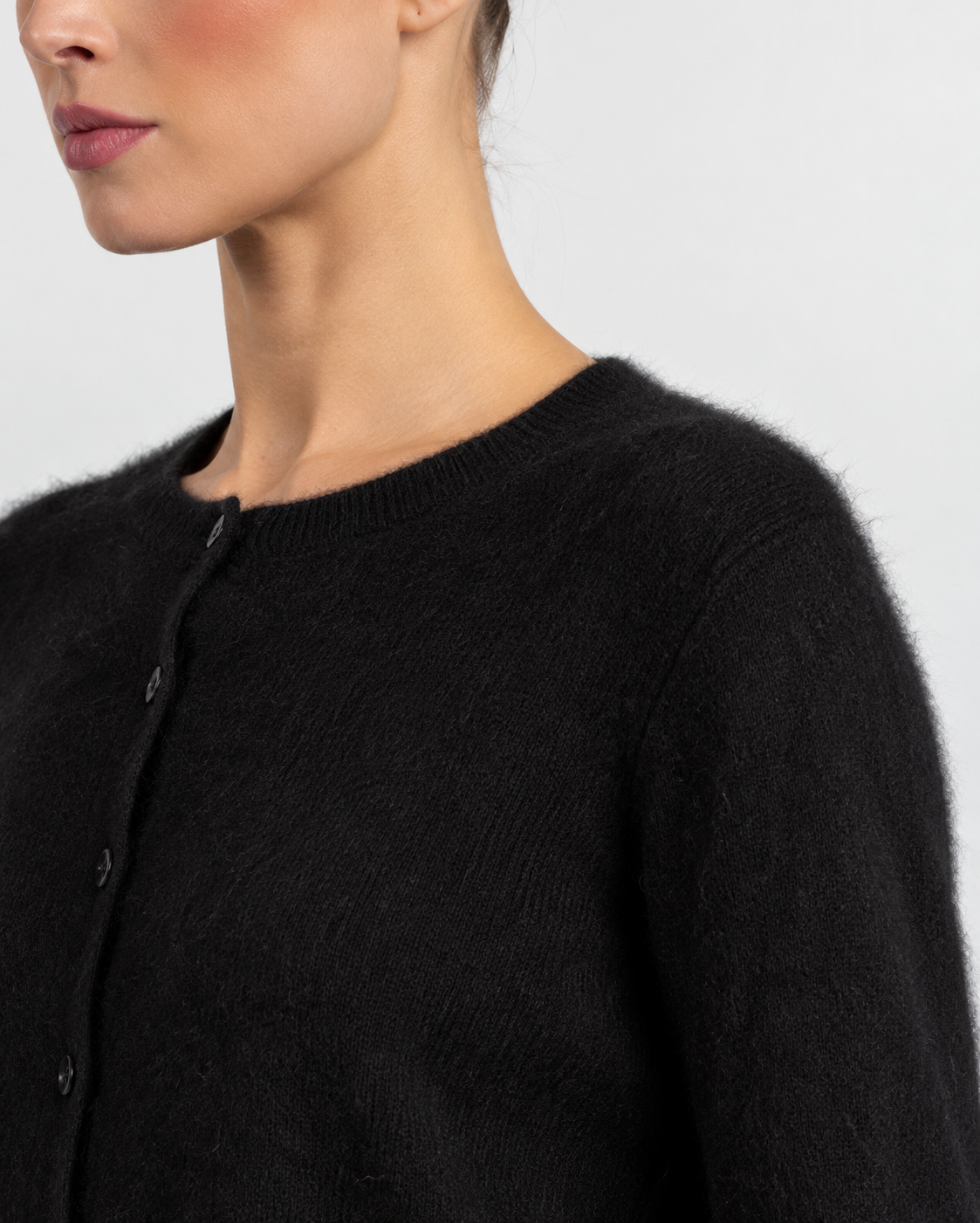 Close-up of a model wearing a fuzzy black knit cardigan sweater with a buttoned front and ribbed crew neckline against a light gray background.