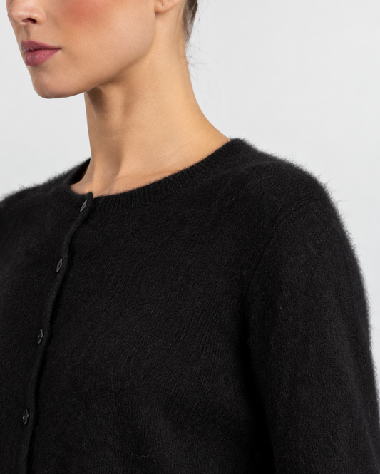 Close-up of a model wearing a fuzzy black knit cardigan sweater with a buttoned front and ribbed crew neckline against a light gray background.