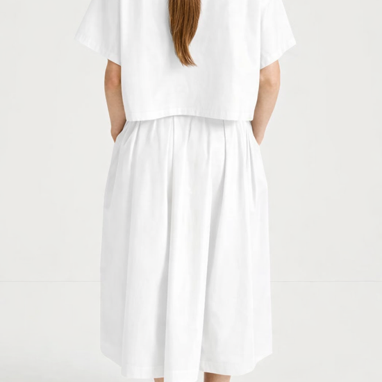 model wearing a white skirt and top outfit facing away 