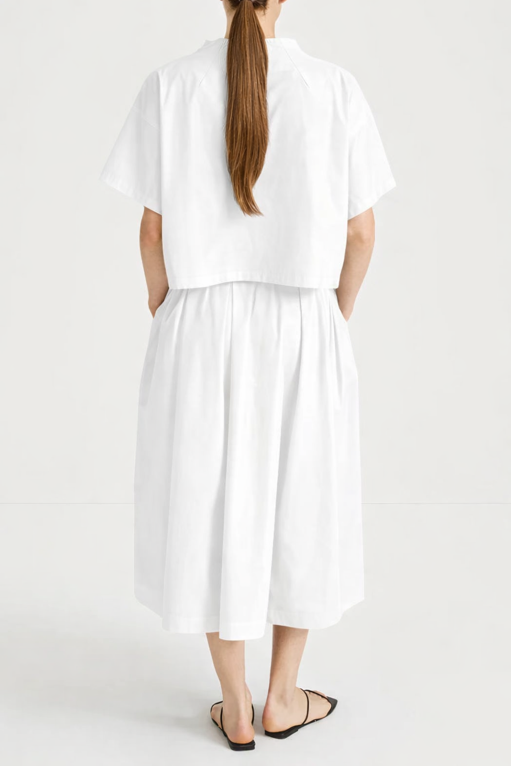 model wearing a white skirt and top outfit facing away 
