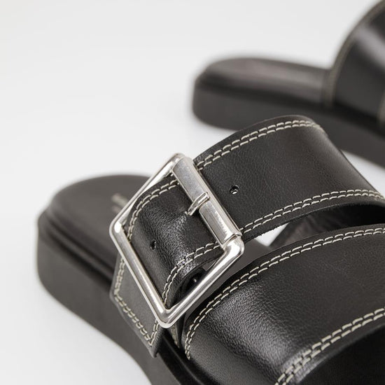 Black leather slider with white stitching and large silver toned buckle