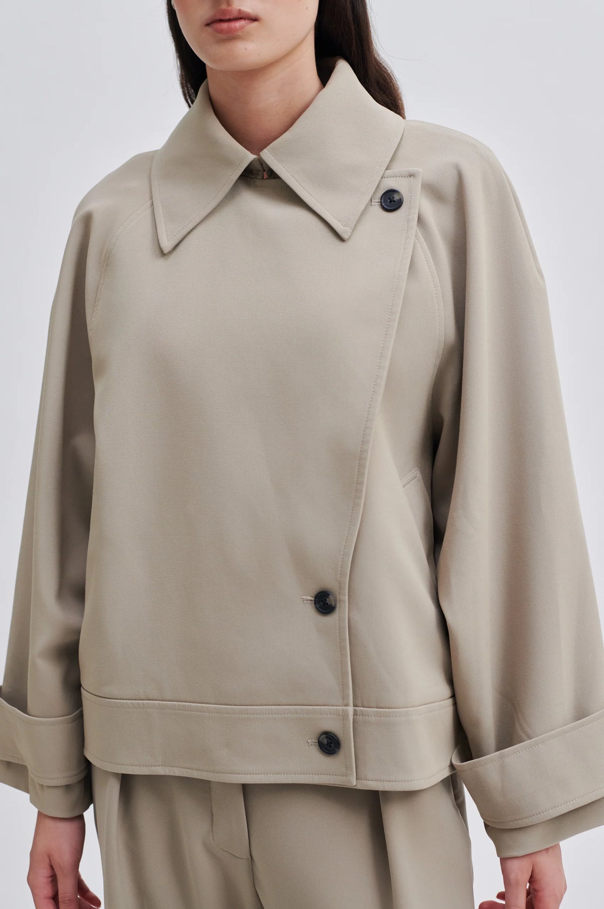 Light taupe short trench jacket with double breasted button fastening large collar raglan sleeves and cuff belts