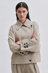 Light taupe short trench jacket with double breasted button fastening large collar raglan sleeves and cuff belts