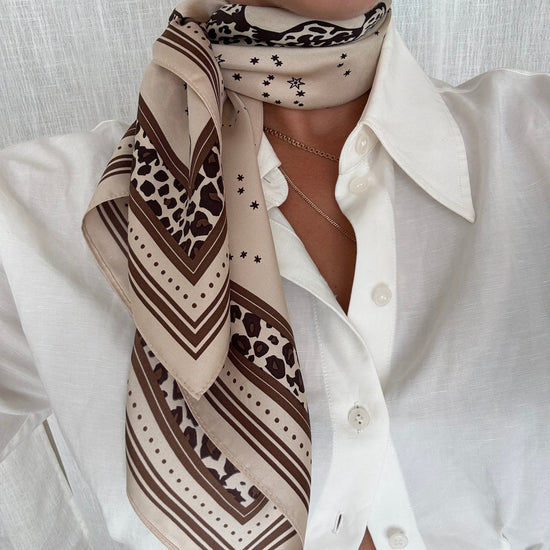 Person wearing a patterned scarf with a white shirt against a neutral background