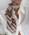 Person wearing a patterned scarf with a white shirt against a neutral background