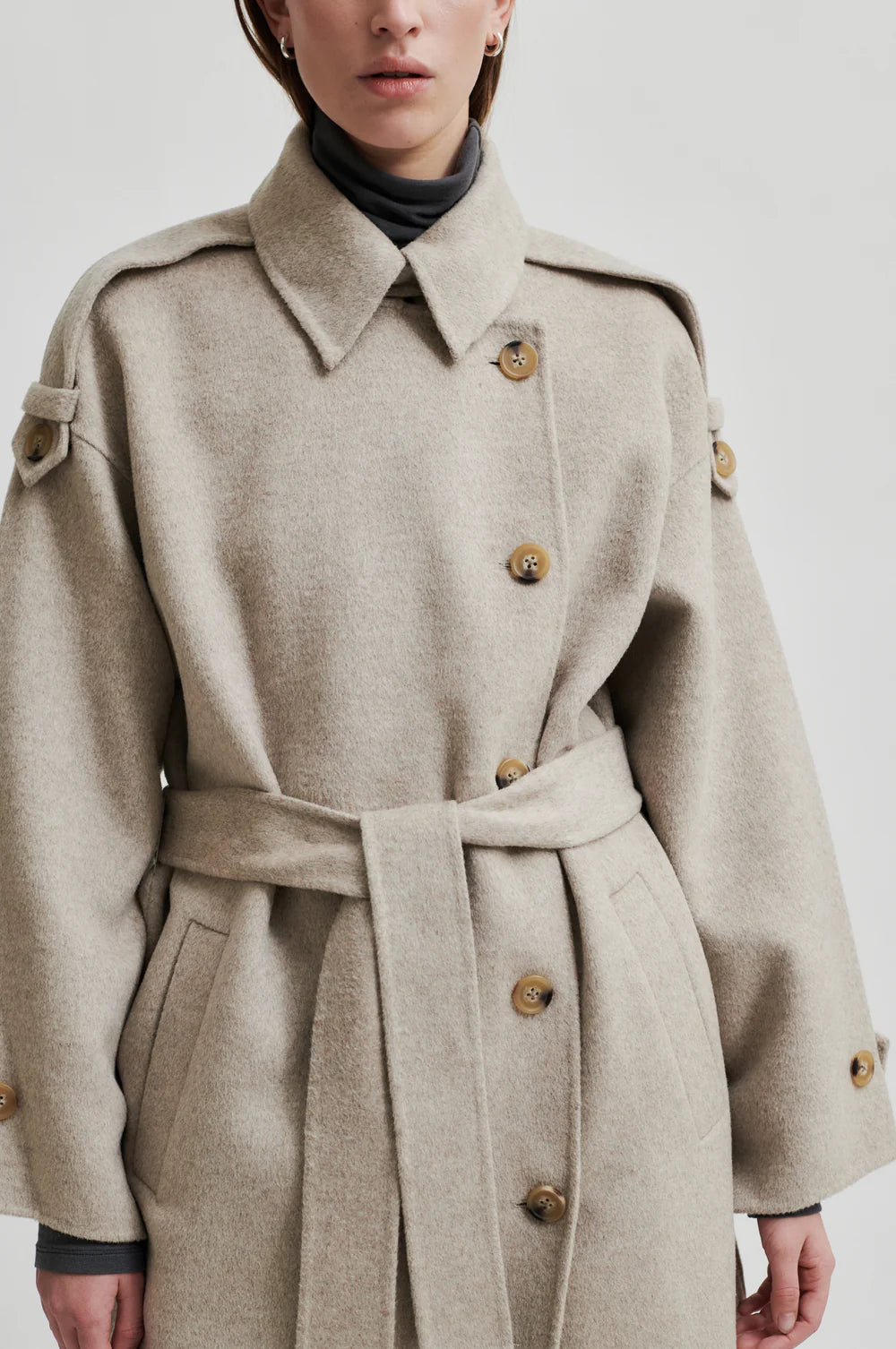 Beige wool double breasted coat with tie waist, asymmetric button fastening and side pockets close up