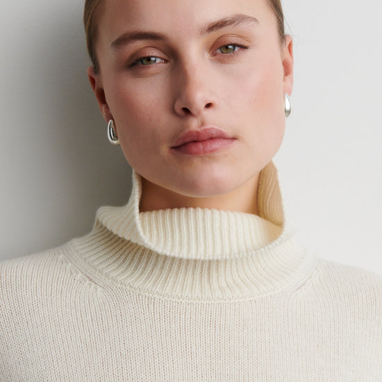 Woman wearing a cream turtleneck sweater against a plain background from Second Female