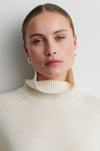 Woman wearing a cream turtleneck sweater against a plain background from Second Female