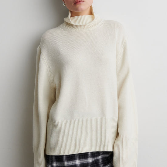 Person wearing a cream sweater and plaid skirt against a plain background from Second Female