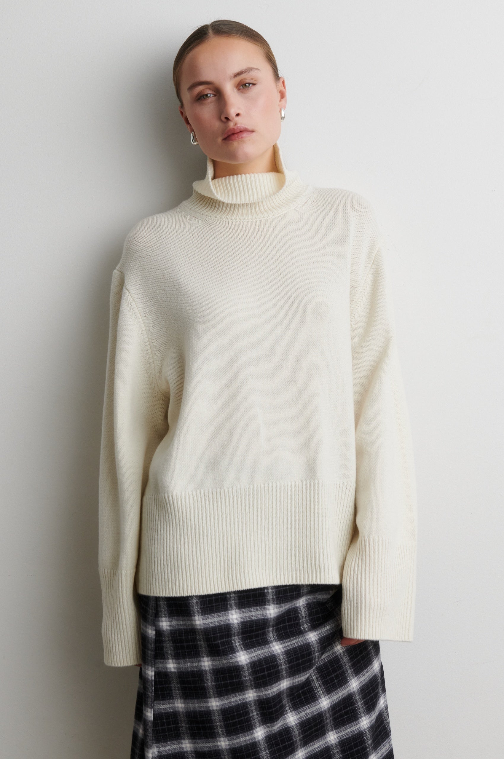 Person wearing a cream sweater and plaid skirt against a plain background from Second Female