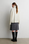 Person wearing a white turtleneck, plaid skirt, and black rain boots against a white wall from Second Female