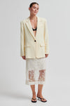 Woman wearing a light yellow blazer over a black bralette and floral skirt on a white background