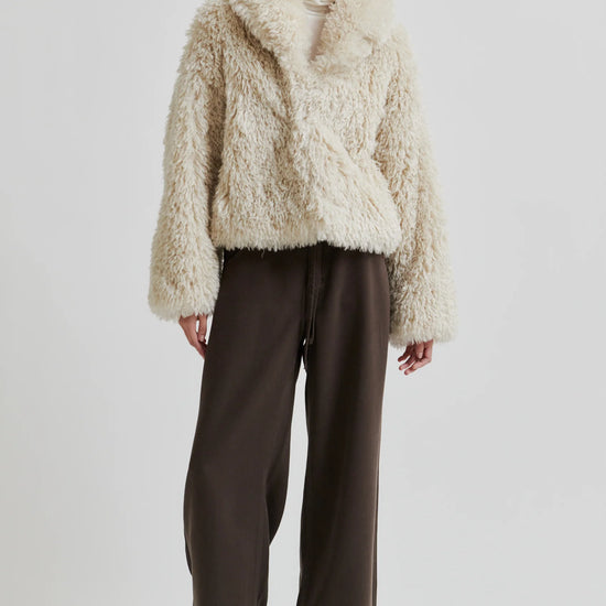 Person wearing a fluffy beige coat and dark pants on a white background