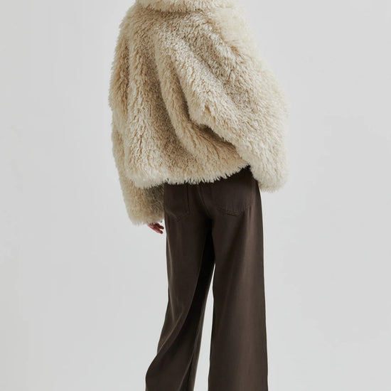 Person wearing a fluffy beige jacket and brown pants on a white background rear view