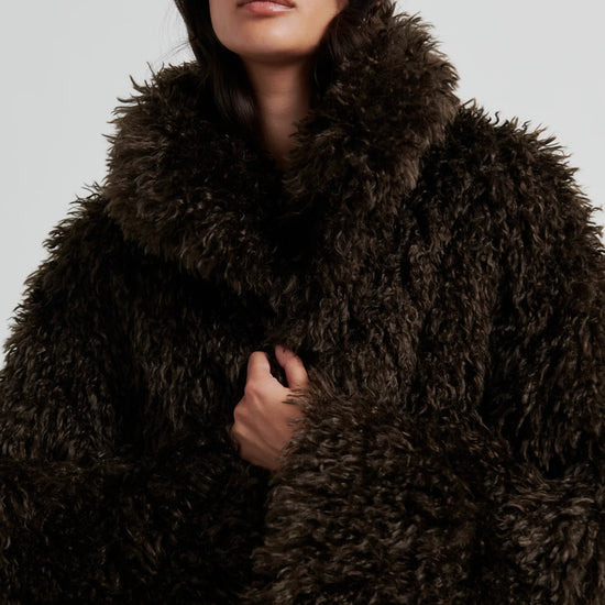 Woman wearing a dark brown fluffy coat against a light gray background