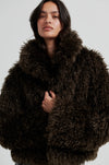 Woman wearing a dark brown fluffy coat against a light gray background
