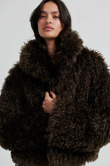 Woman wearing a dark brown fluffy coat against a light gray background