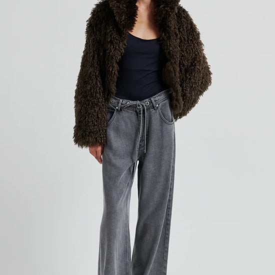 Woman wearing a brown fur coat, black top, and gray jeans on a white background