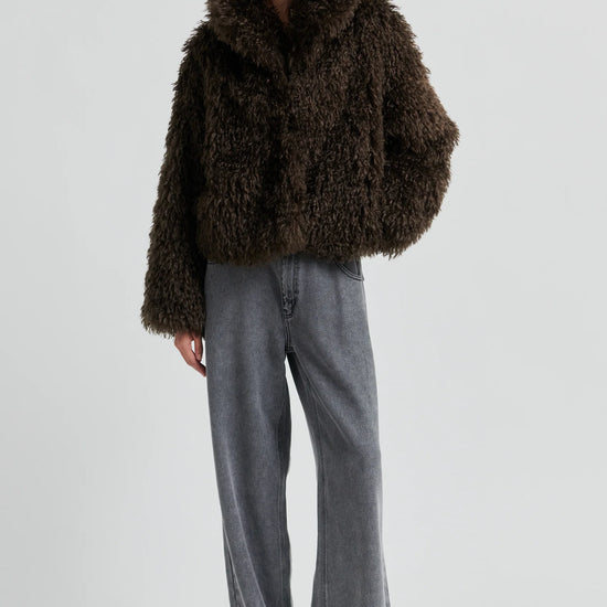 Person wearing a brown fluffy coat and gray pants on a white background