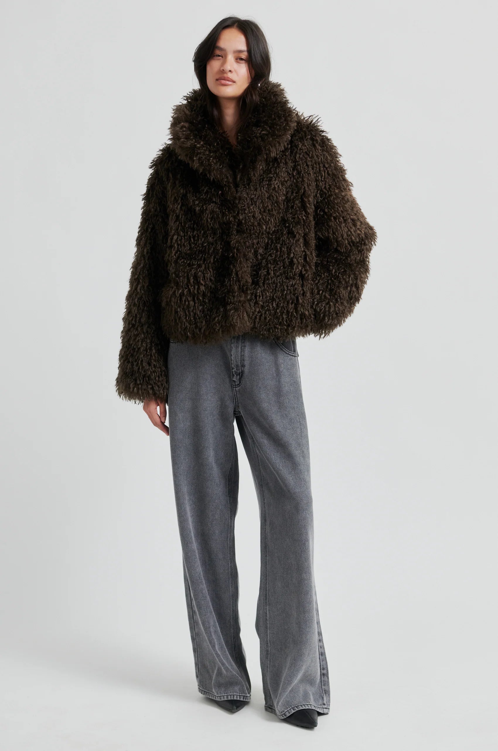 Person wearing a brown fluffy coat and gray pants on a white background