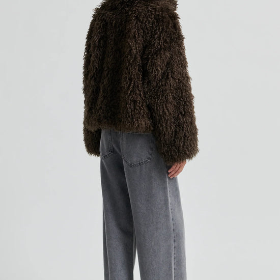 Person wearing a brown fluffy coat and gray pants on a white background