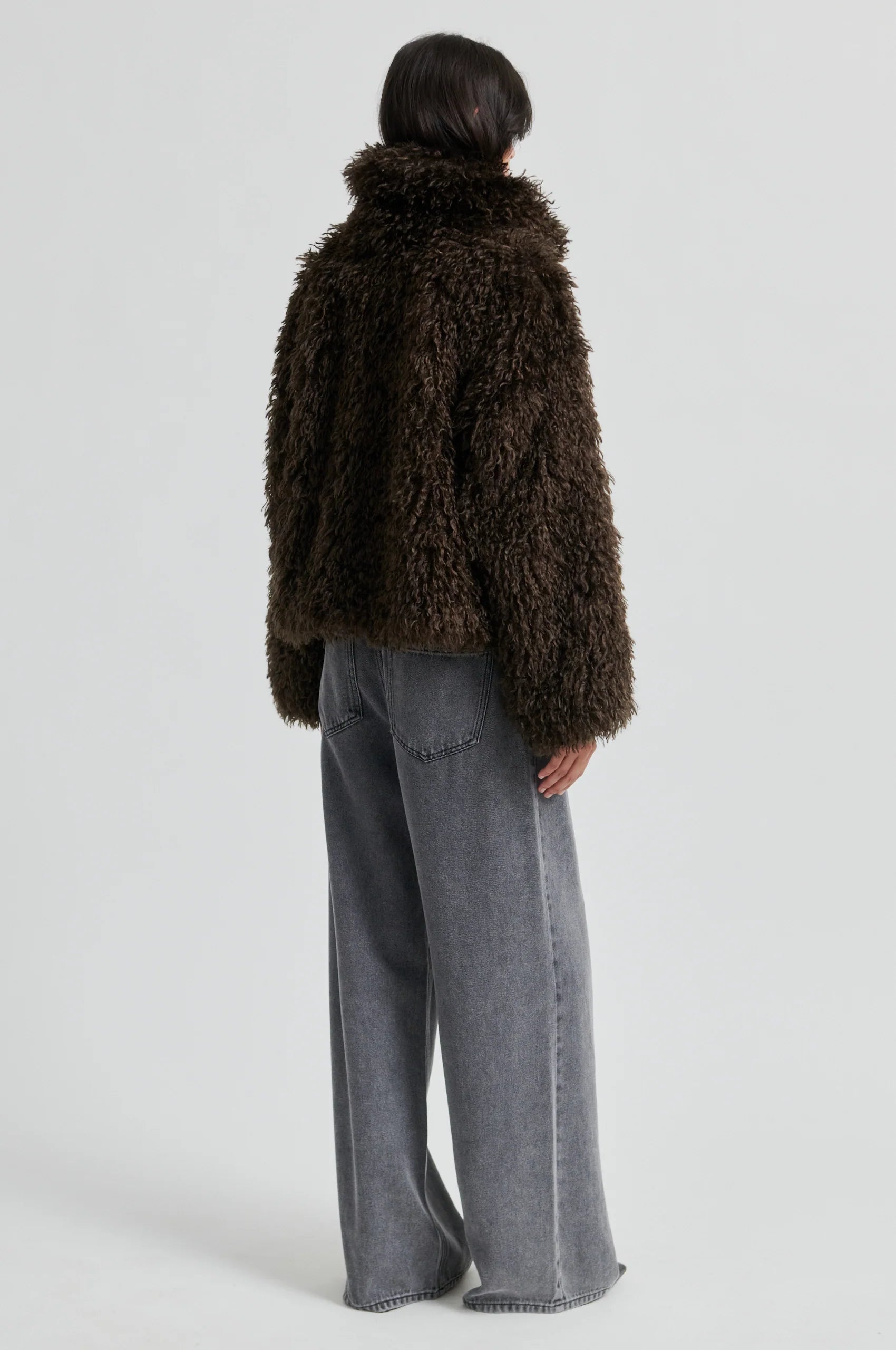 Person wearing a brown fluffy coat and gray pants on a white background