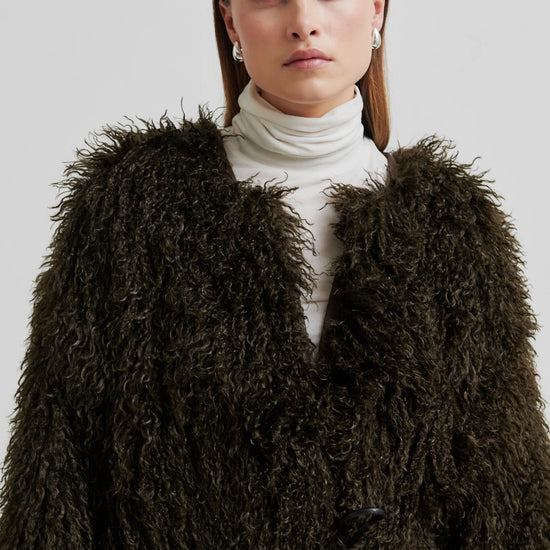 Woman wearing a brown fluffy coat against a plain background