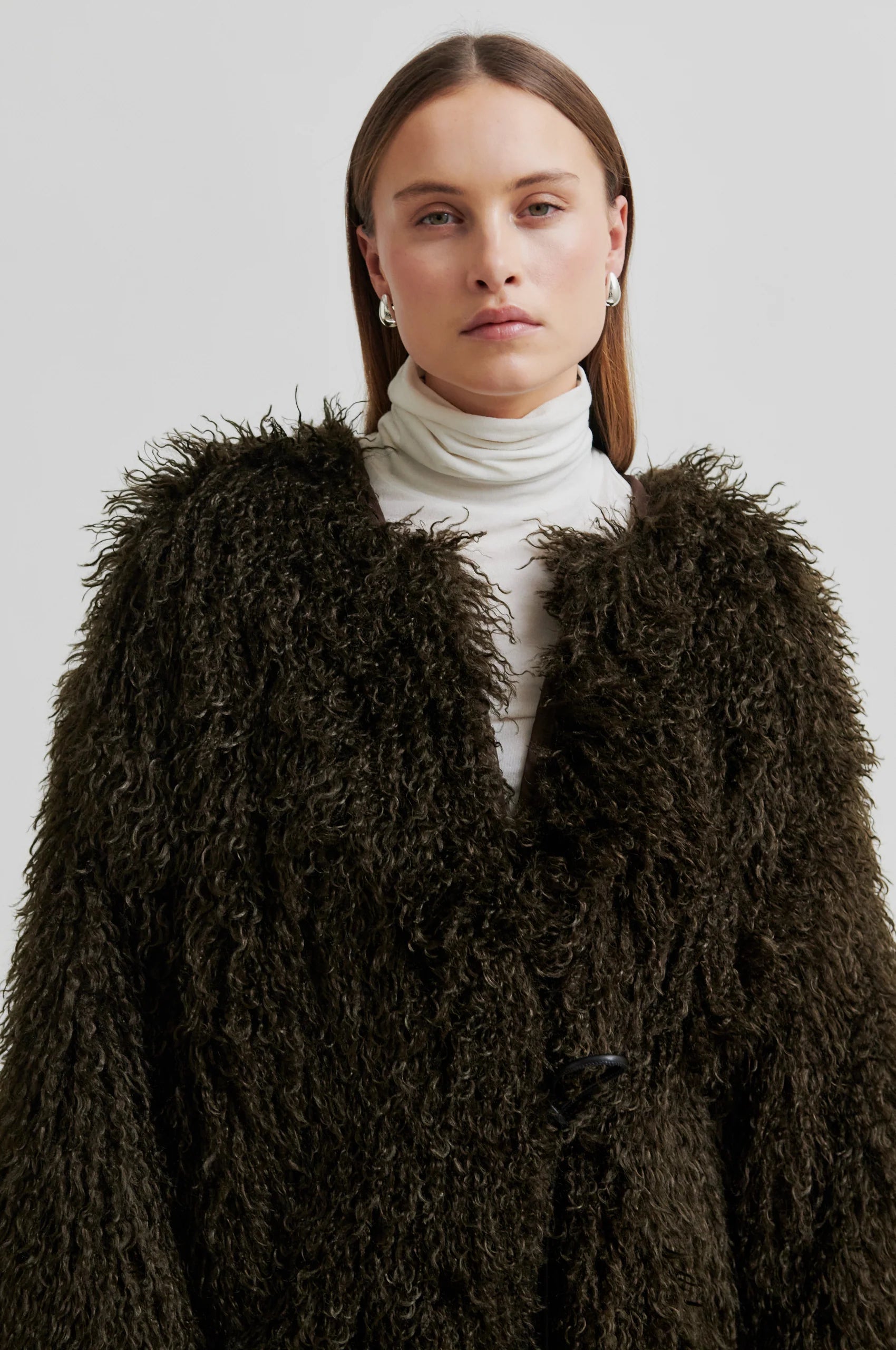 Woman wearing a brown fluffy coat against a plain background