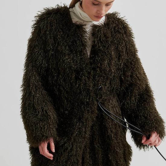 Woman wearing a long, dark brown fluffy coat against a plain background