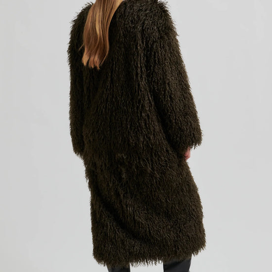 Person wearing a long, dark brown fur coat on a light gray background
