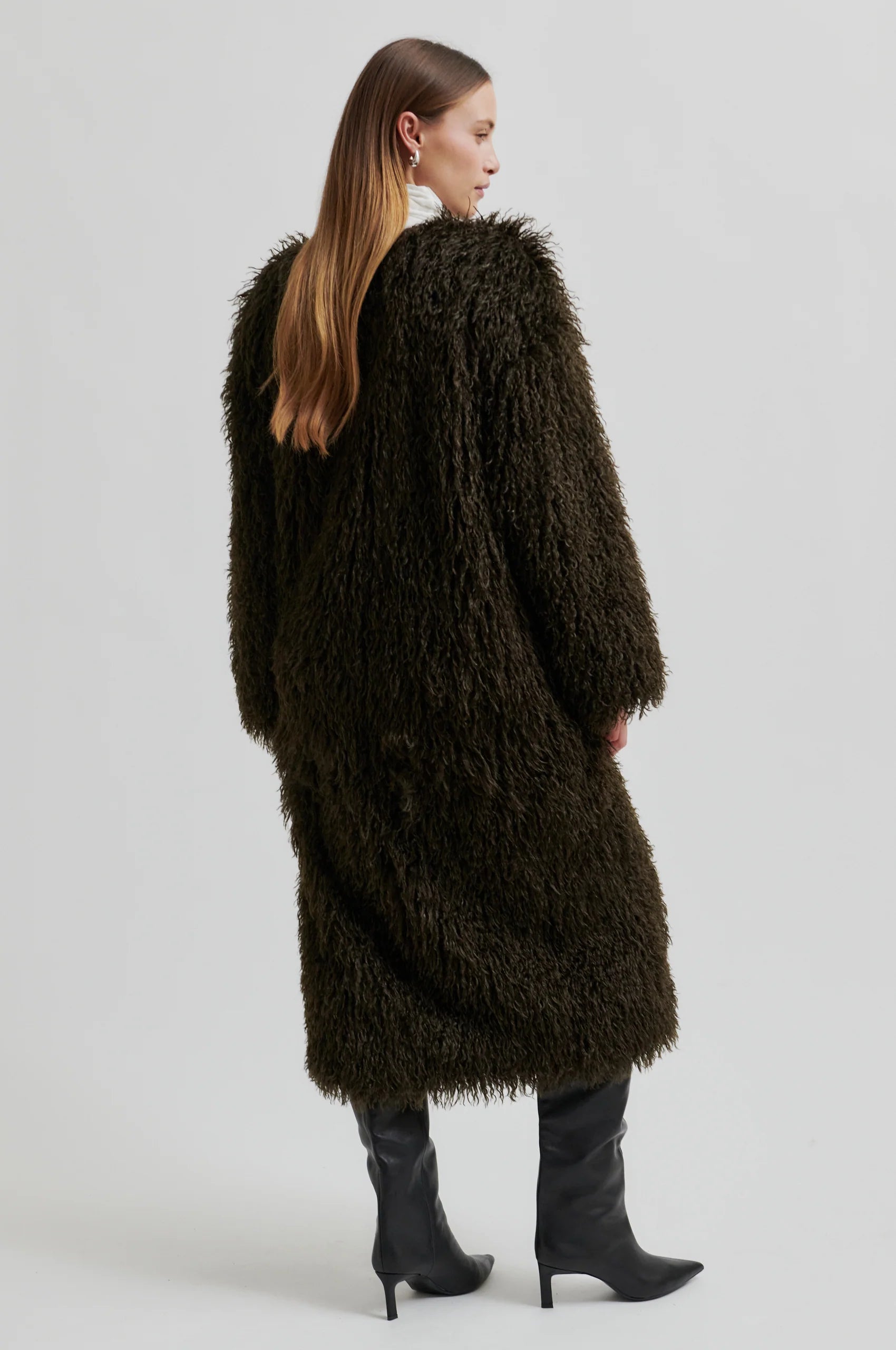 Person wearing a long, dark brown fur coat on a light gray background